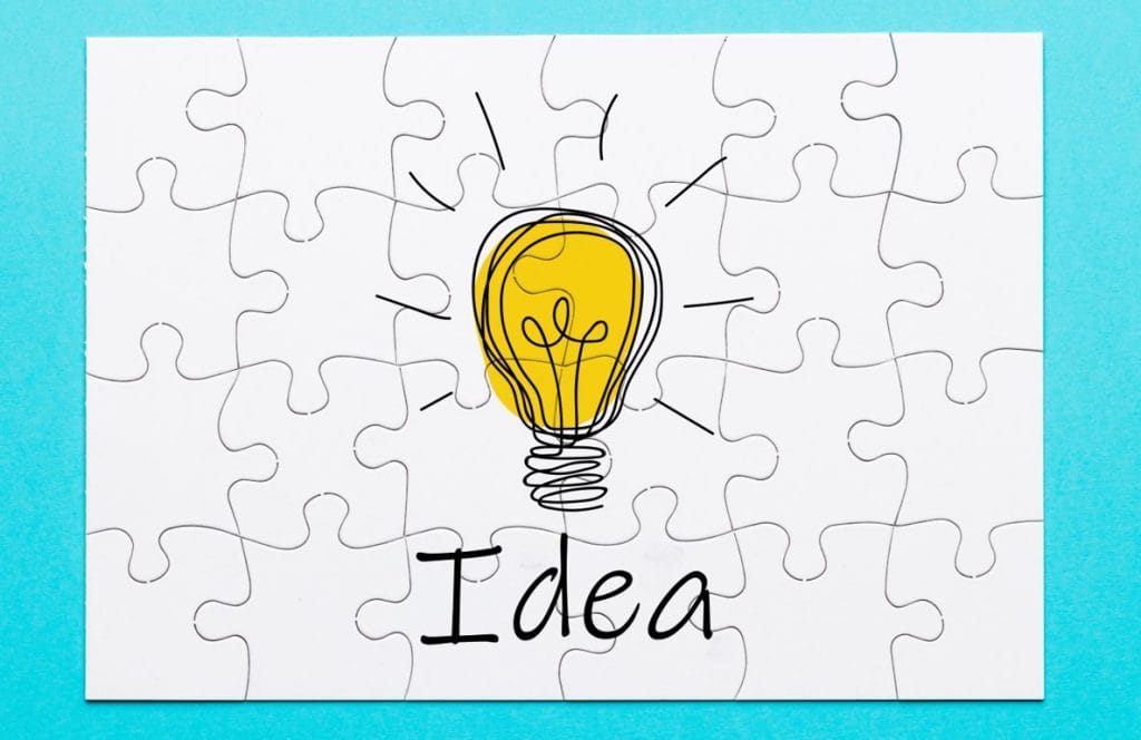 idea Lightbulb on with "idea" written under it in a white puzzle background with teal outline