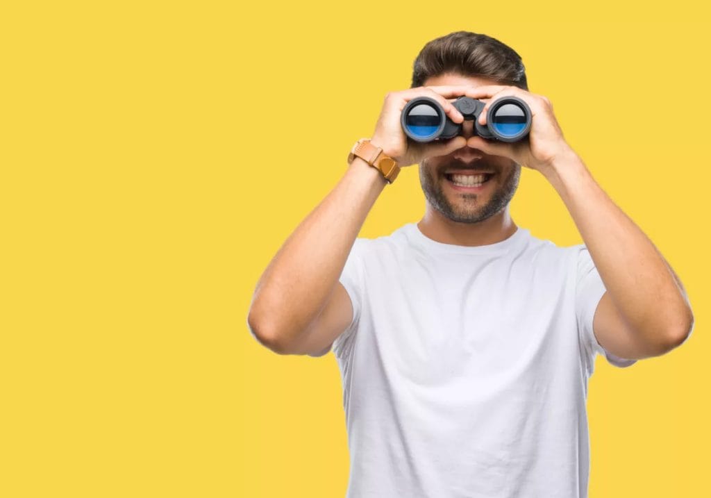 Young,Handsome,Man,Looking,Through,Binoculars,Over,Isolated,Background,With