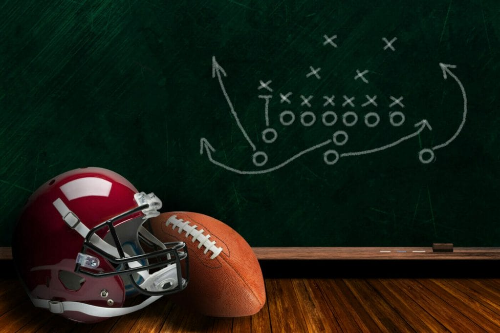 Football,Helmet,And,Ball,With,Play,Strategy,Drawn,On,A Football and helmet in front of black board